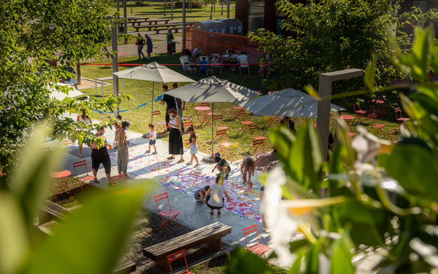 Bambini e adulti dipingono un grande telo colorato all'aperto alla Cascina, tra ombrelloni e sedie rosse