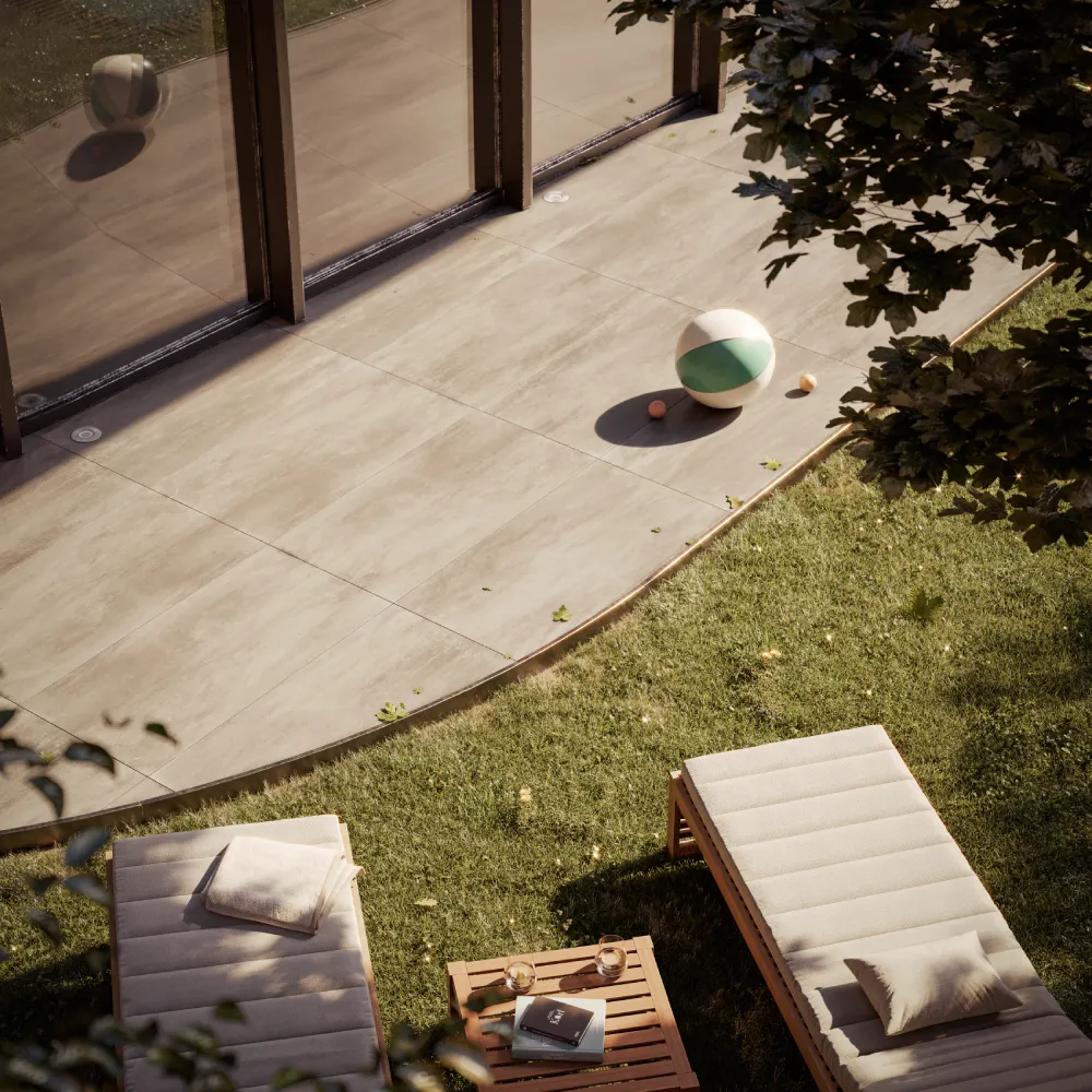 Terrazza pavimentata e prato con due lettini prendisole e un tavolino, accanto a una vetrata